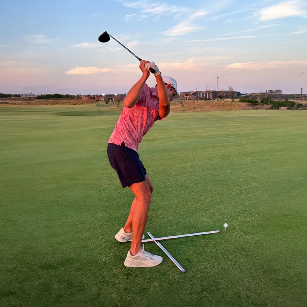 Golfer using T Alignment training aid practicing golf on a green course with a clear sky.